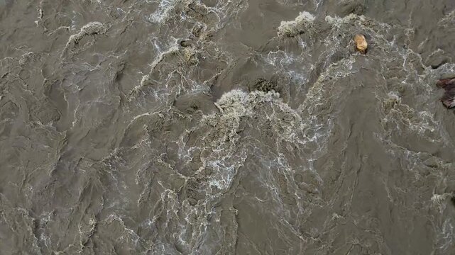 Extreme close up view of swirling muddy river water creating white foam and complex ripples on the surface during monsoon season in Nepal