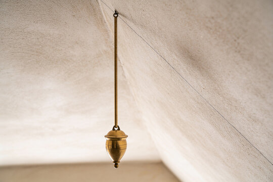 Brass plumb bob hanging against a rough plastered wall