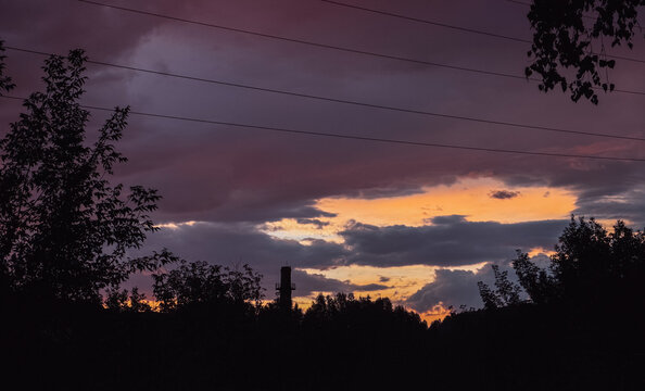 Purple storm clouds over city silhouettes at sunset, dramatic evening sky.