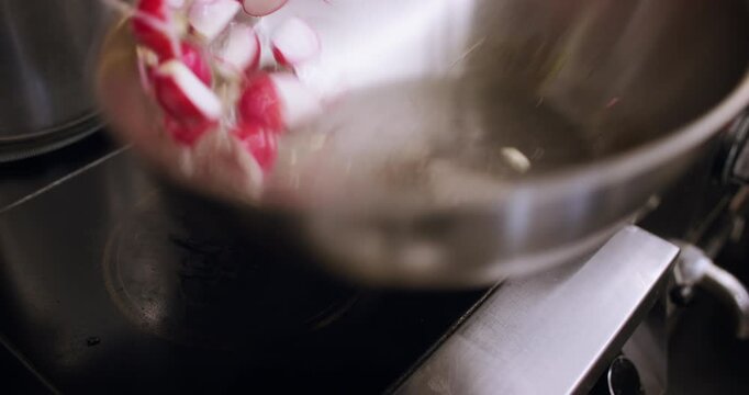Roasting food. Frying vegetable. Male chef hand adding radish garlic piece to hot oil tossing metal pan preparing tasty spicy dish.