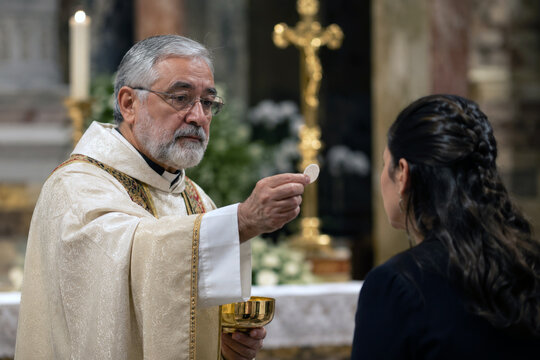 A priest extends communion bread during a sacred service, with warm church light and shallow focus emphasizing the ceremonial moment. Christian worship and sacramental devotion concept