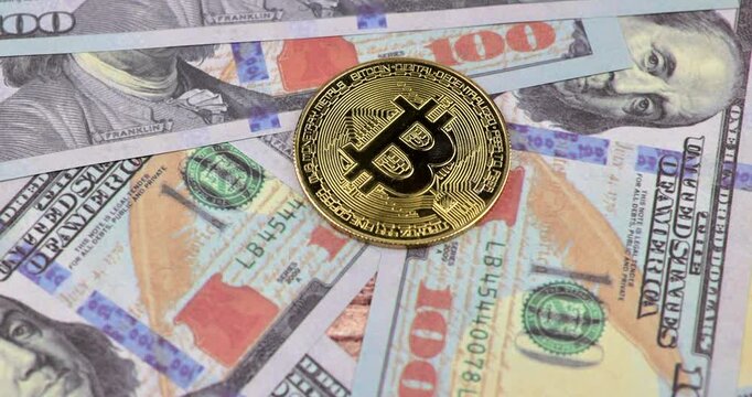 Horizontal close up showing human hand stacking multiple shiny physical bitcoin tokens in a precise row on top of US hundred dollar paper currency bills.