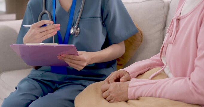Asian nurse writes notes on clipboard and gestures while consulting senior Asian woman, documenting health discussion and providing daily nursing support in senior care center for healthy aging.