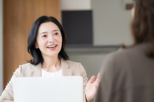 笑顔で顧客と対面相談する50代女性、オフィスで説明や提案を行うビジネスウーマン　コミュニケーションや商談などのビジネスイメージ