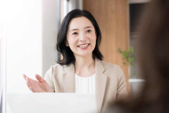笑顔で顧客と対面相談する50代女性、オフィスで説明や提案を行うビジネスウーマン　コミュニケーションや商談などのビジネスイメージ
