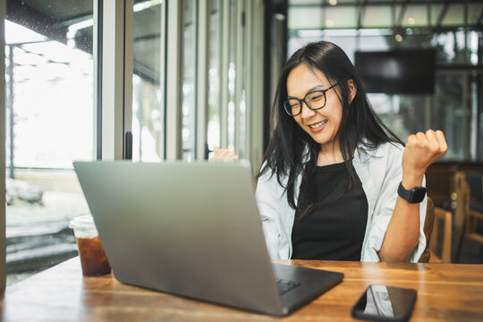Happy woman celebrating a successful achievement while working on a laptop in a modern cafe, representing business success, productivity, career growth, accomplishment and professional achievement.
