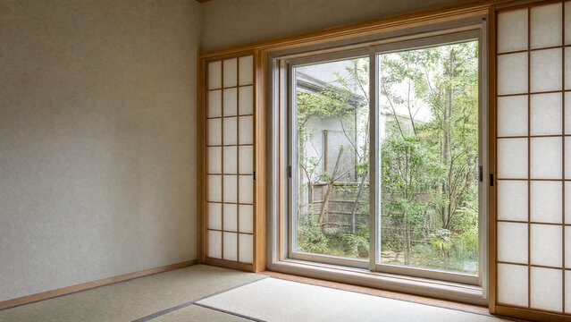 Empty Japanese tatami room with shoji screens and a sliding glass door to a garden