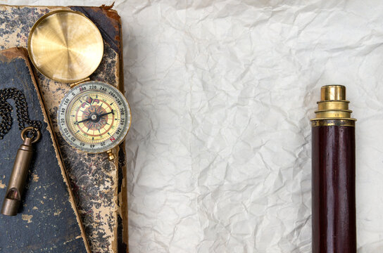 Vintage brass compass, spyglass telescope and whistle on old books with crumpled paper background. Travel adventure and exploration concept. Retro navigation tools with copy space for text.