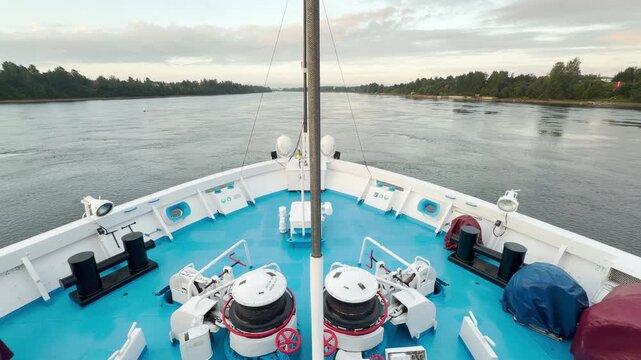 A cruise ship sails smoothly along the tranquil river. Empty chairs line the deck under a gentle sky. Passengers feel peaceful and relaxed in the calm atmosphere.