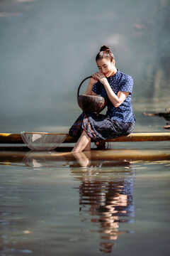 happy Asian women in traditional indigo dress catching fish on a bamboo bridge in Sakon Nakhon, Thailand. Perfect for travel banners and culture ads.