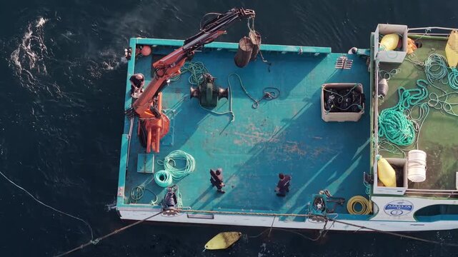 Fishing crew operate a deck crane lifting heavy gear on a workboat off Conil de la Frontera.