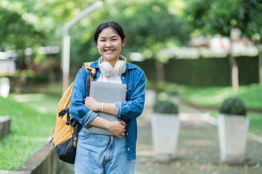 Young asian student smiling holding laptop on campus