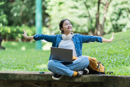 Young woman enjoying freedom and nature in park with laptop