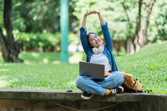 Student stretching arms while studying outdoors in park