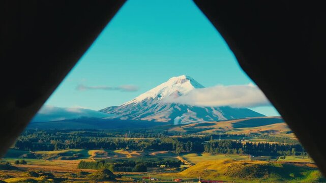 Cotopaxi volcano viewed through a triangular wooden frame with rolling hills and clouds below in Ecuador
