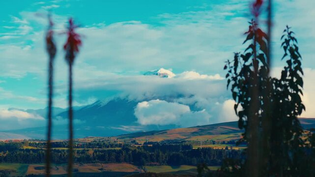 Cotopaxi volcano emerges from clouds above a lush valley in Ecuador