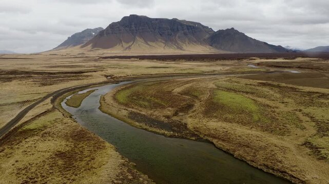 Markarfljot River winds below Einhyrningur Mountain in Rangarthing eystra, South Iceland, Iceland, crossing glacial outwash terrain beneath volcanic slopes, drone descent.