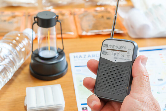 Person holding portable emergency radio with hazard map and disaster preparedness supplies