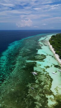 Vertical drone descends and orbits left while tracking a boat departing Dumaluan Beach across reef waters in Panglao, Bohol