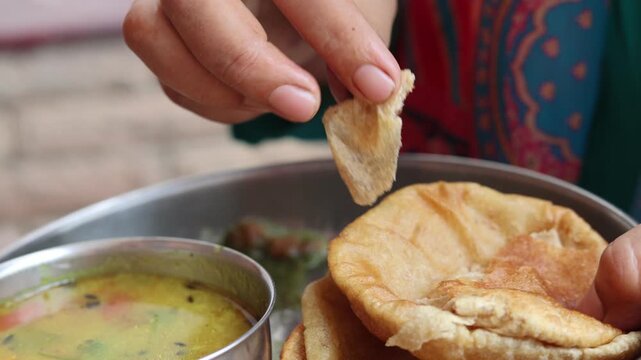 Close-up of Indian food being eaten by hand with puri and curry, representing traditional eating habits, homemade food and rural Indian cuisine.