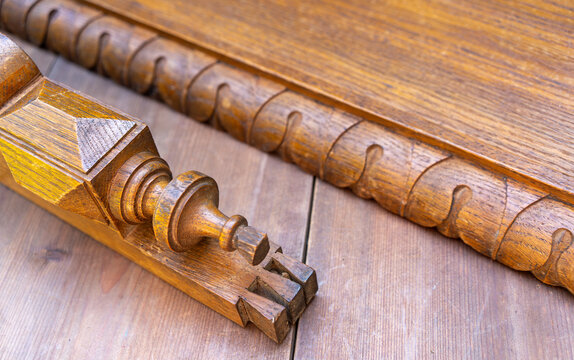 Closeup of antique carved wooden furniture parts with broken spindle and decorative molding lying on wood floor. Restoration and repair of old vintage furniture. Craftsmanship and joinery concept.