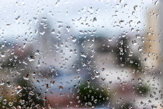 Close-up of water drops on a glass window pane during a rainy day in Brazil, creating a textured surface with a colorful soft blurred city background.