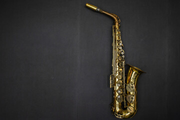 Fototapeta premium Golden alto saxophone on vintage dark leather background. Classic brass alto saxophone placed horizontally on a clean dark black textured leather background, 