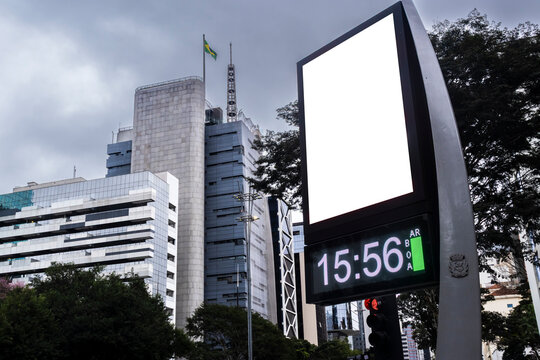 Digital billboard with blank white mockup display on Paulista Avenue. A modern street clock with an isolated white screen frame for advertisement placement, 
