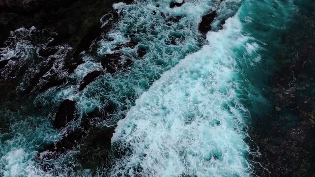 Cinematic high-angle view of waves crashing against the rocks.