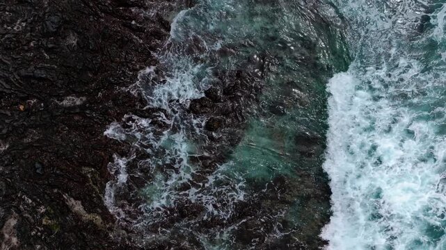 Cinematic high-angle view of waves crashing against the rocks.