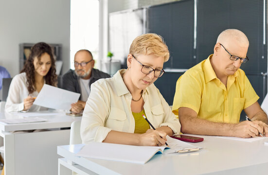 Adults students in classroom writing notes. Focused mature group attends training for continuing education and completes tasks in a bright room. Clear concept career learning and reskilling.