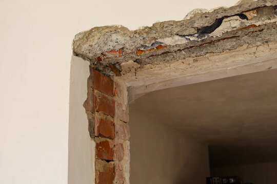 Dismantled doorway showing exposed red brickwork and a concrete lintel during renovation. Preparation of an interior wall opening for installing new entrance or interior doors. Demolition process of a