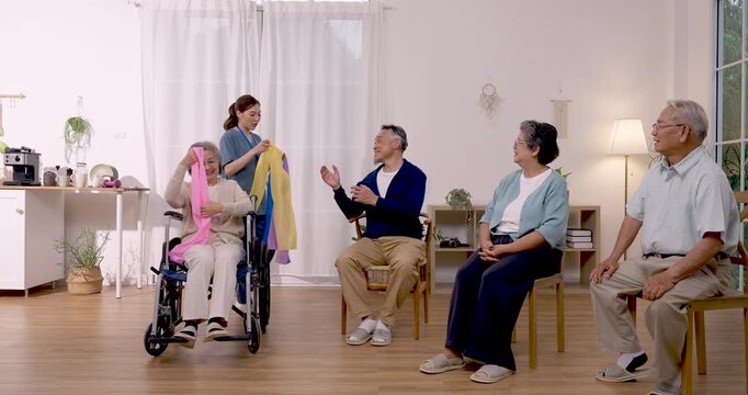 Asian nurse distributes resistance bands and assists senior Asian residents preparing for seated rehabilitation exercise inside senior care center, supporting safe mobility training and healthy aging.