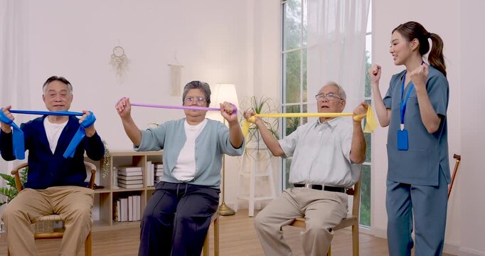 Senior Asian group stretches resistance bands at chest level while Asian nurse guides seated rehabilitation exercise inside assisted living community, supporting strength, mobility and healthy aging.