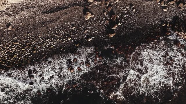 Cinematic high-angle view of waves crashing against the rocks.