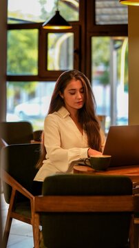 Young woman focused on her laptop while enjoying coffee in a cozy cafe setting