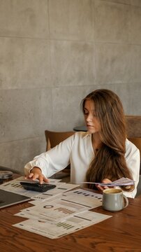 Young woman calculating finances with papers and calculator at a wooden desk