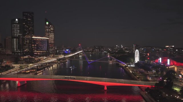 A wide night aerial view shows the Victoria and Neville Bonner Bridges plus the illuminated Wheel of Brisbane along the riverfront.
