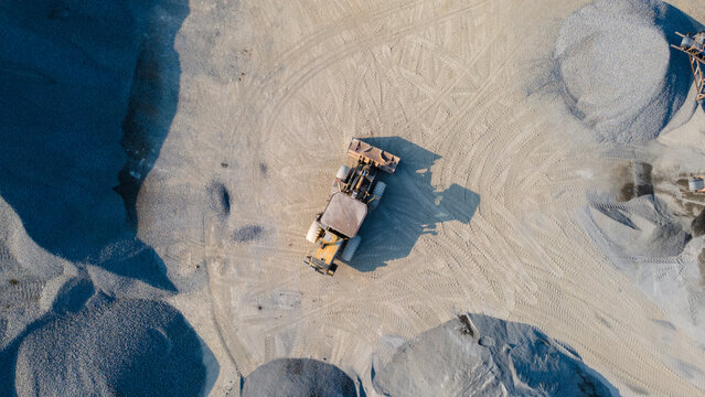 Wheel Loader in the Middle of an Aggregate Stockpiling Area. Heavy Construction Machinery Surrounded by Rock, Sand, and Processed Materials at an Industrial Mining Site view from above.