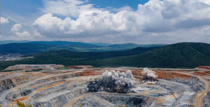 Aerial view of open pit mine with active mining operations and explosive detonation