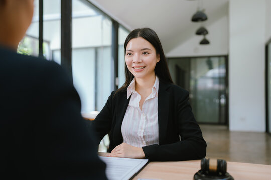 Asian businesswoman discussing a legal or corporate agreement with a colleague during a professional meeting, symbolizing negotiation, consulting, and business law.