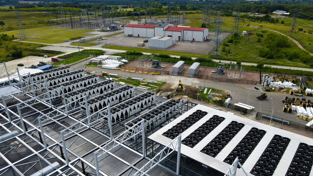 Large data center building under construction featuring extensive rooftop cooling units and an adjacent electrical substation providing essential power for global network infrastructure