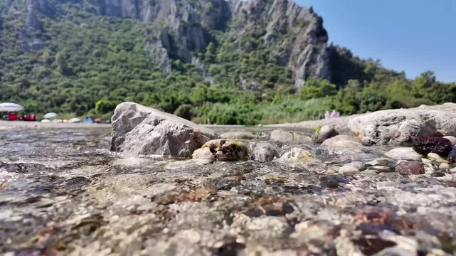 Clear mountain stream flowing over rocks with mountain landscape in slow motion