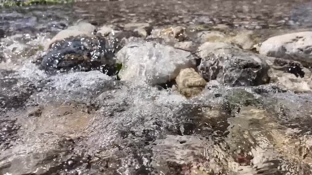 Fresh mountain stream cascading over rocks in bright sunlight, slow motion