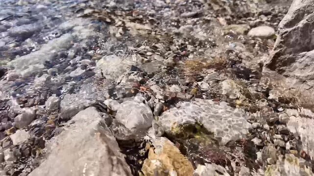 Sunlit stream water gliding between natural rocks and pebbles in a detailed slow motion close-up