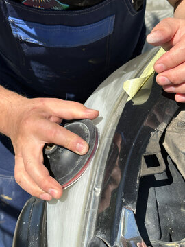 Close-up of a craftsman's hands sanding a plastic car headlight in Gomel. Masking tape protects edges. Active preparation of equipment for the autumn-winter season, August 28, 2026.