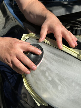 Close-up of a craftsman's hands sanding a plastic car headlight in Gomel. Masking tape protects edges. Active preparation of equipment for the autumn-winter season, August 28, 2026.
