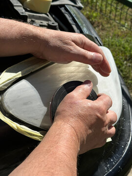Close-up of a craftsman's hands sanding a plastic car headlight in Gomel. Masking tape protects edges. Active preparation of equipment for the autumn-winter season, August 28, 2026.