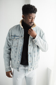 Young Black man wearing a denim jacket and black turtleneck, looking
