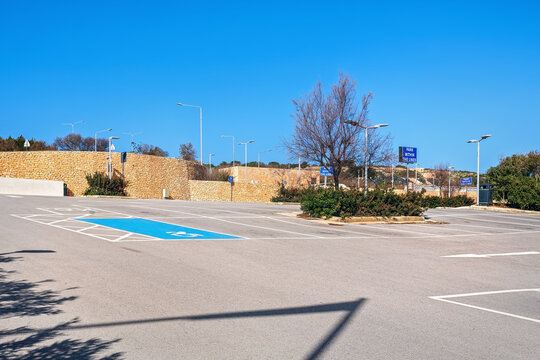 Empty asphalt parking lot with blue handicap accessible marking, park within lines signs, stone wall under clear sky